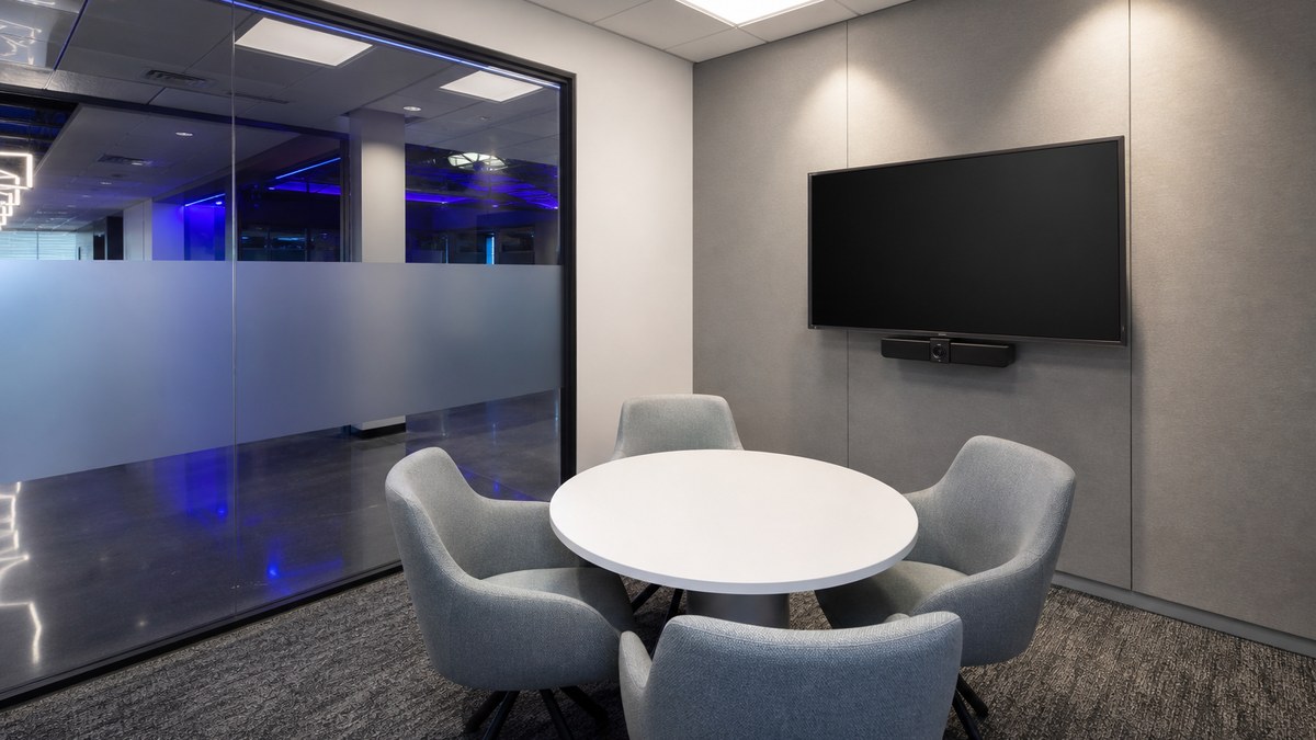Small huddle room in a Plano office suite with low-glare LED panel lighting, wall lighting and a video conferencing screen